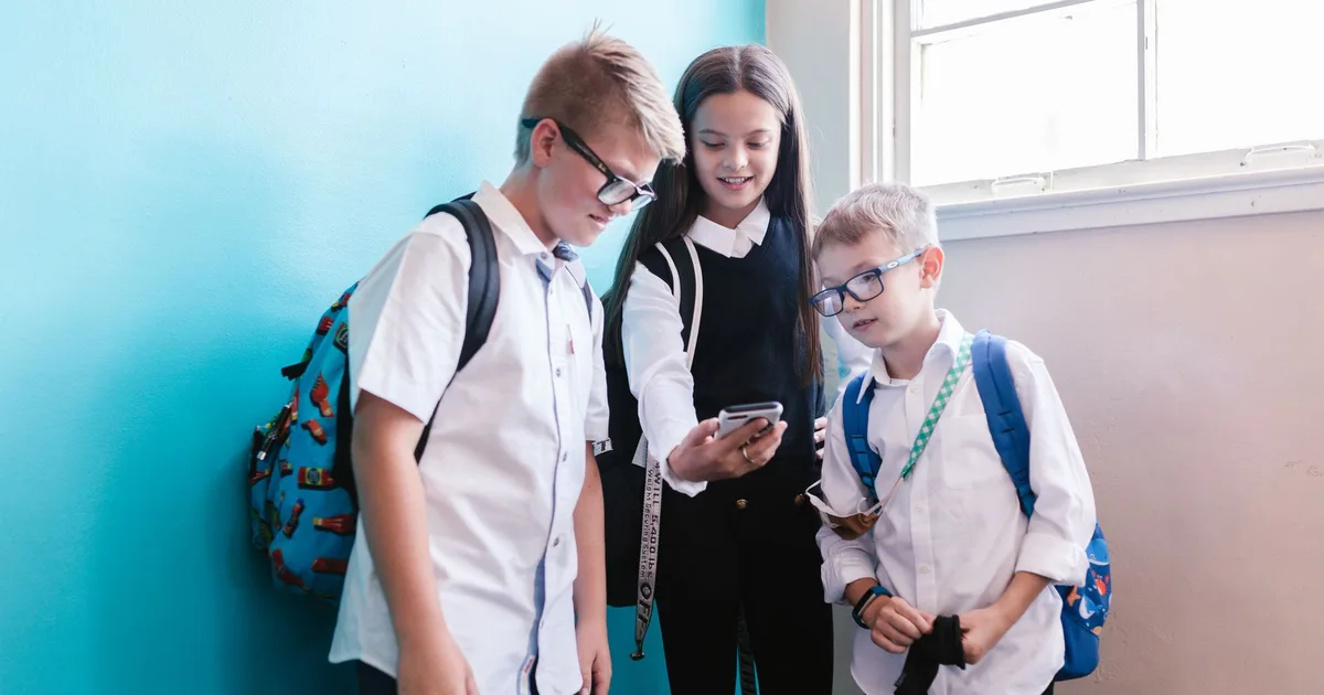 Niña con morral de colegio usando su primer celular, la escena que define qué celular para niños comprar en Colombia en 2026.