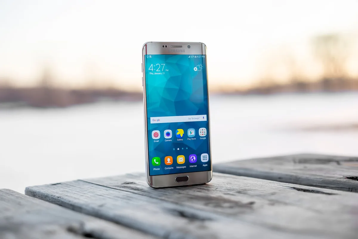 Celular Samsung apoyado sobre una mesa de madera al aire libre.